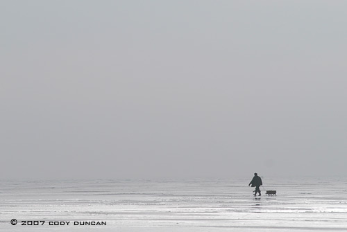 © cody duncan photography. Ice fisherman walking on frozen curonian lagoon, lithuania
