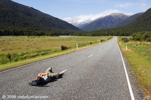 New Zealand travel photography: person lying in empty road near Haast Pass. © Cody Duncan Photography