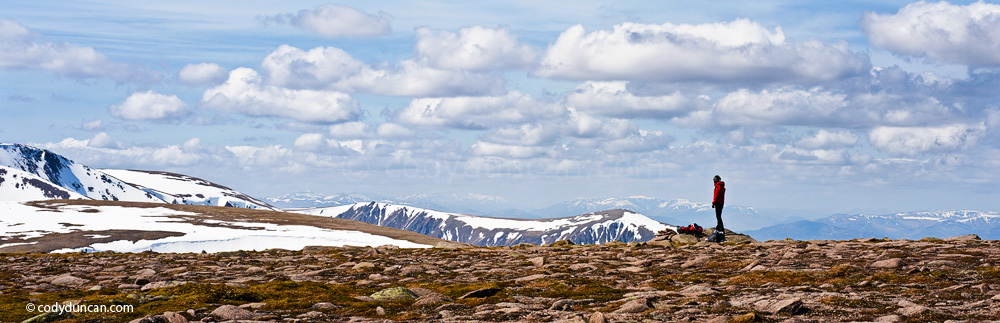 Panoramic stock photography: Female hiker takes in view of Cairngorm mountains from near summit of Cairn Lochan, Scotland