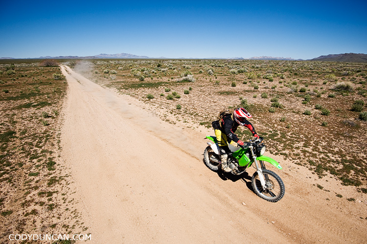 Dual sport motorcycle rides through desert along Mojave trail road, California